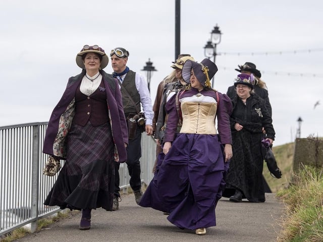 Dressed up guests walking along Whitby beach at Whitby Steampunk Weekend.