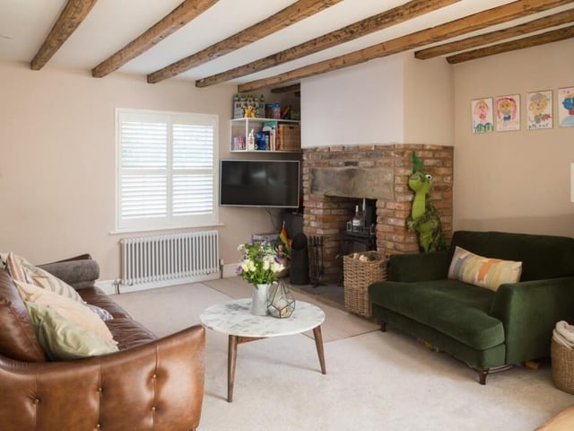 A beamed reception room with feature fireplace of exposed brick, and a log burner.