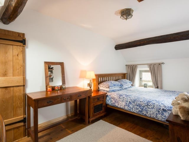 A beamed double bedroom with wood flooring.