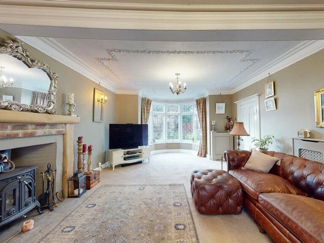 A comfortable lounge with bay window, feature fireplace with stove, and decorative detail to the ceiling.