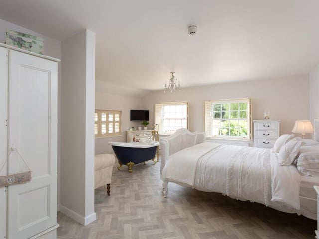A large and bright bedroom with a free-standing, claw foot bath.