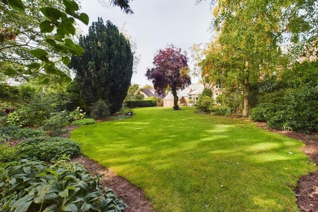 The attractive garden has a variety of trees, plants and shrubs around its shaped lawn.
