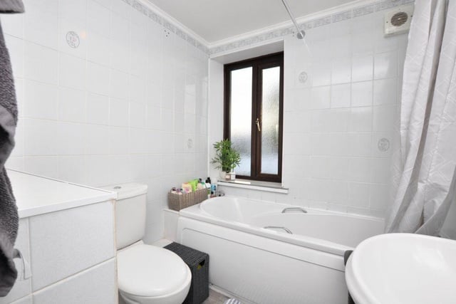 A white tiled bathroom, with bath and overhead shower.