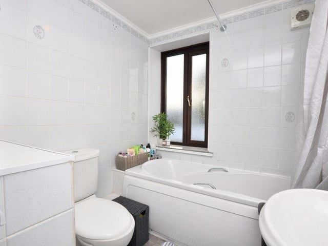 A white tiled bathroom, with bath and overhead shower.