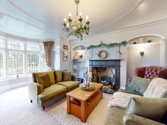 A bay windowed reception room with open fireplace and fitted shelving.