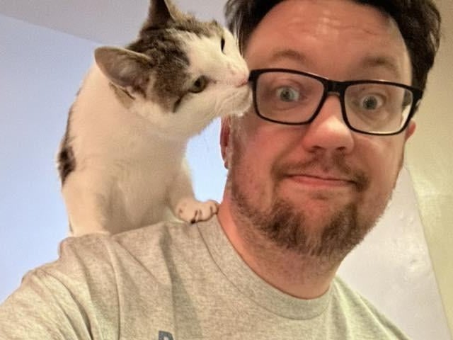 A previously reluctant cat dad with his beloved pet, who is taking a chance trying to chomp on glasses!